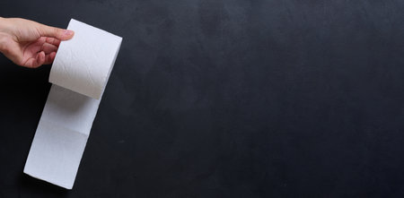 A female hand holds a roll of white toilet paper against a black background. Copy spaceの写真素材