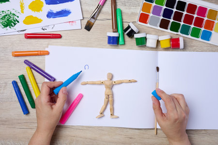 Set of watercolor paints, brushes and paper with different strokes and colors. Female hands holding a felt-tip penの写真素材