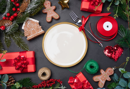 Empty round white plate with fork and wrapped gifts with Christmas decor on a black background. Festive backgroundの写真素材