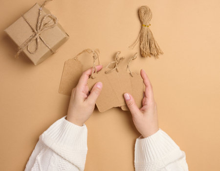 Rectangular brown paper price tags with ropes are held by female hands, top viewの写真素材