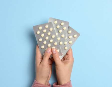 Two female hands holding round pills in a blister pack on a blue background, top viewの写真素材