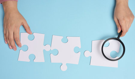 White empty puzzles and a magnifying glass in hand on a blue background, top viewの写真素材
