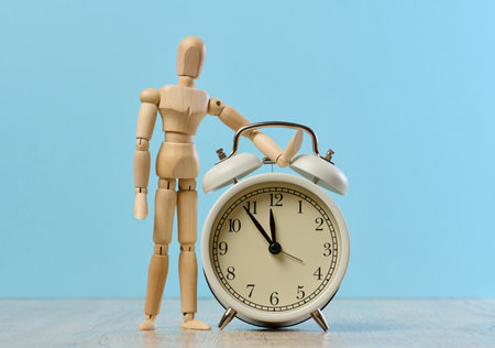 Wooden mannequin standing next to an alarm clock.の写真素材