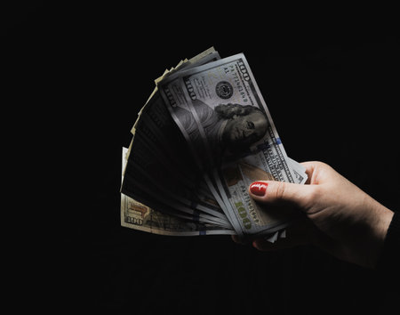 Female hand holding one hundred dollar American bills on a black backgroundの写真素材