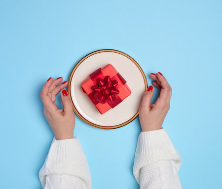 Two female hands holding a plate with a gift on a blue background, top viewの写真素材