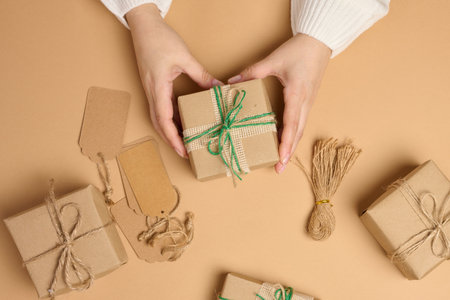 Female hands holding a gift box on a beige background. View from above