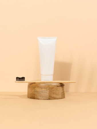 White plastic toothpaste tube and wooden toothbrush on a beige background.