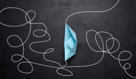 A blue paper boat and a tangled trajectory drawn in chalk. The concept of difficult decisions, a long way and overcoming difficultiesの写真素材