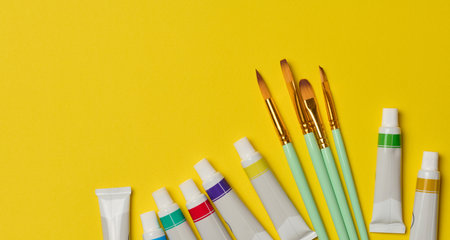 Tubes with oil paint and brushes on a yellow background, top viewの写真素材