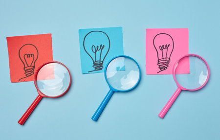 Drawn light bulbs on sheets of paper and a plastic magnifying glass, the concept of searching for...