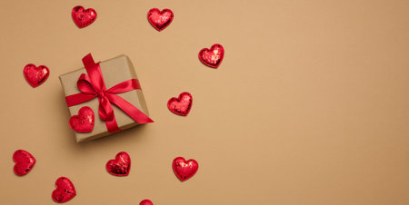 Box tied with a red ribbon and small hearts on a beige background, top view. Copy spaceの写真素材