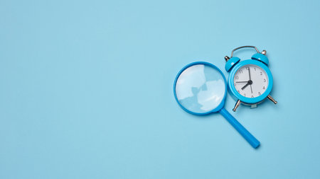 Alarm clock and magnifying glass on a blue background, symbolizing the concept of a deadline. Copy spaceの写真素材