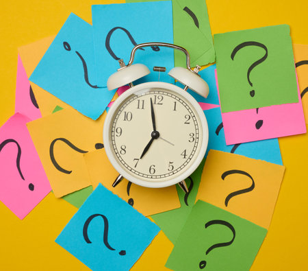 A round alarm clock amidst paper stickers featuring drawn question marks, symbolizing the concepts of truth-seeking and deadlines.の写真素材