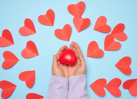 A woman's hand holds a red rubber heart on a blue background, symbolizing the concept of donation...