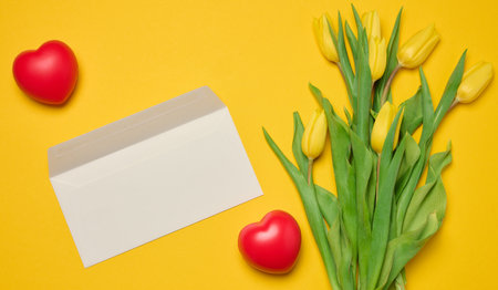 Envelope and red heart and bouquet of blooming tulips with green leaves on a yellow background, top viewの写真素材