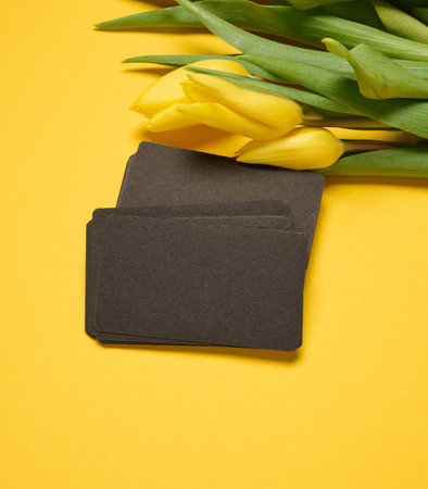 Blank paper black business card and a bouquet of yellow tulips on a yellow background, close upの写真素材