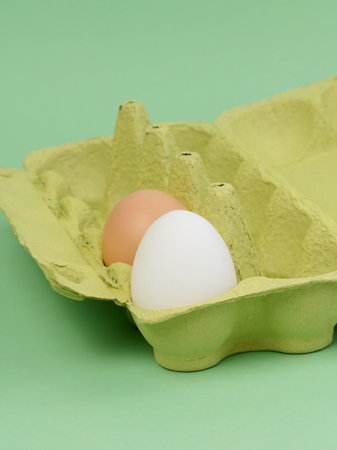 Two chicken eggs in a paper box on a green background, close upの写真素材