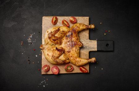 Whole fried chicken with spices on a wooden board on a black table, top viewの写真素材