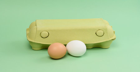 Two chicken eggs in a paper box on a green background, close upの写真素材