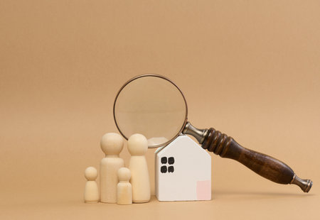 Magnifying glass and a family of wooden figures on the background of a house, the concept of searching for real estate rental, mortgageの写真素材