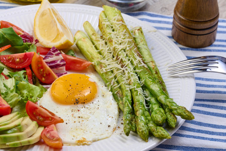 Round plate with cooked asparagus, fried egg, avocado and fresh vegetable salad on the table, top viewの写真素材