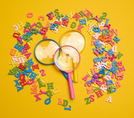 Plastic magnifying glass and wooden letters of the English alphabet on a yellow background, top viewの写真素材