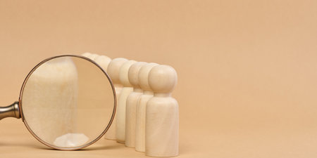 Wooden figures of men stand on a beige background and a wooden magnifying glass. Recruitment concept, search for talented and capable employees, career growthの写真素材