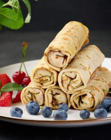 Stack of fried crepes with filling on a round plate, black tableの写真素材