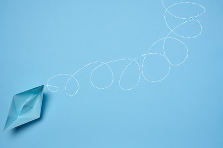 Blue paper boat and a long tangled path, symbolizing the concept of a challenging journey, top viewの写真素材