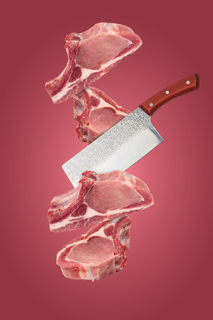 Raw pieces of pork on the bone and a cutting knife levitate on a red backgroundの写真素材