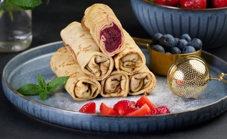 Crepes stacked in a pile, one of which is cut and filled with berry filling. The plate decorated with blueberries, black backgroundの写真素材