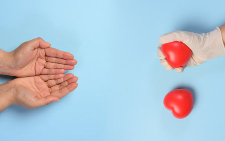A woman's hand holds a red rubber heart on a blue background, symbolizing the concept of donation
