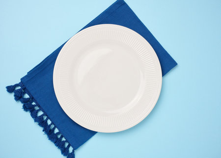 Round ceramic empty white plate and blue linen kitchen towel top viewの写真素材
