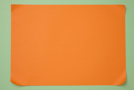 Blank orange sheet of paper on green background, abstract backdrop for inscription, copy spaceの写真素材