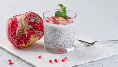 Glass with chia and yogurt dessert decorated with fresh fruits and pomegranate seeds on white tableの写真素材