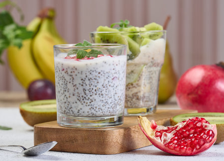 Two glasses of chia yogurt dessert garnished with fresh fruit, pomegranate seeds and kiwi slicesの写真素材