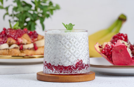 Glass with chia and yogurt dessert decorated with green mint leaf on white tableの写真素材