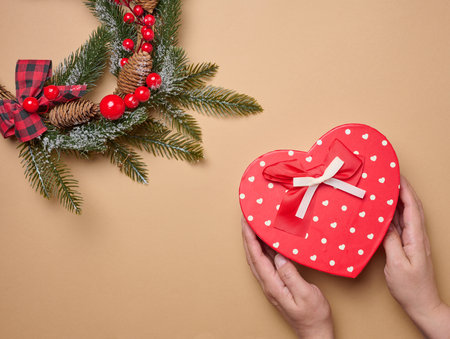 Female hands holding a cardboard red heart-shaped box, top view. Christmas giftの写真素材