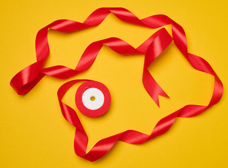 Spool of red silk ribbon on yellow background, top viewの写真素材