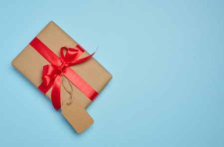 The box is wrapped with red ribbon and brown craft paper with a tag on a blue background, top viewの写真素材