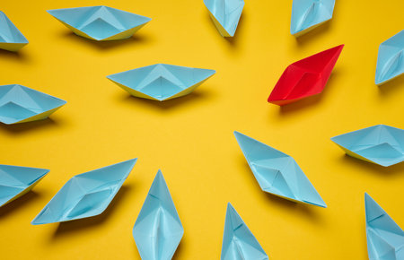 A group of blue paper boats surrounded by one red boat, the concept of bullying, search for compromiseの写真素材