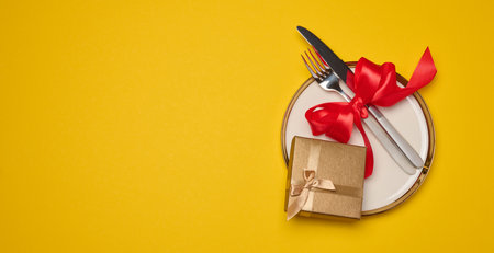 Round plate and tied fork with knife on yellow background, festive table setting. Copy spaceの写真素材