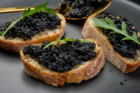 Three pieces of crispy bread with luxurious black caviar and fresh arugula, served on a stylish black plateの写真素材