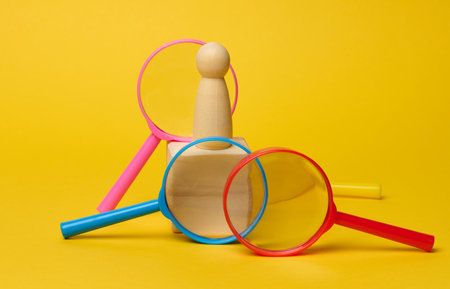 Wooden figurine on cube and plastic magnifying glass on yellow background, talent and employee search conceptの写真素材