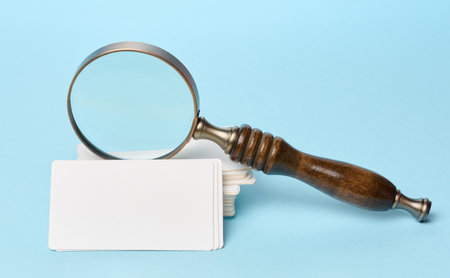 Stack of blank paper white business cards and magnifying glass on blue backgroundの写真素材