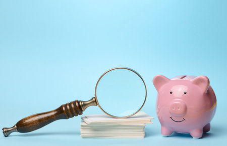 Ceramic piggy bank, stack of business cards and magnifying glass on blue backgroundの写真素材