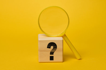 Plastic magnifying glass on yellow background and wooden cube with question mark, information searchの写真素材