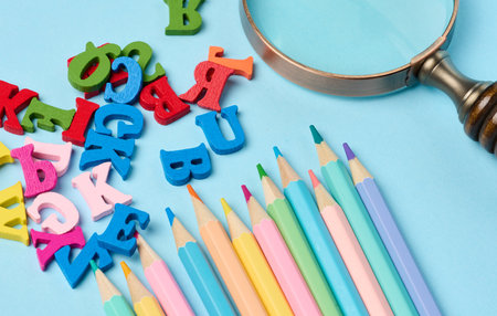 Multicolored wooden pencils and letters on a blue background, close up
