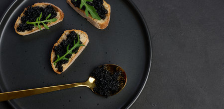 Three pieces of crispy bread with luxurious black caviar and fresh arugula, served on a stylish...