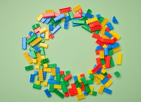 Scattered plastic multi-colored parts of children's construction set on green background, top view